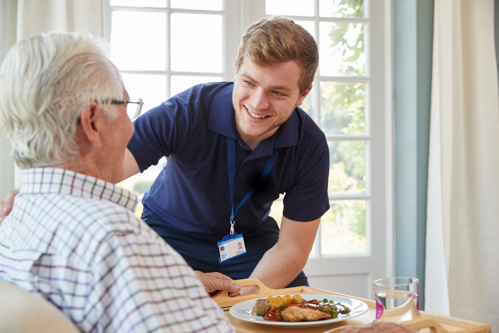 Male,Care,Worker,Serving,Dinner,To,A,Senior,Man,At